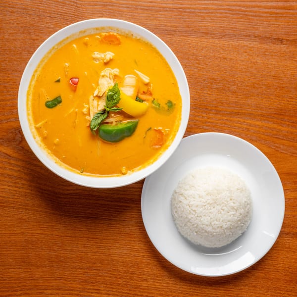 Overhead view of a bowl of red Thai curry with chicken and vegetables, served with white rice.