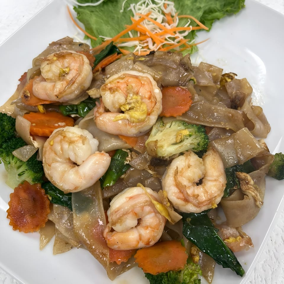 Thai Pad See Ew with shrimp, broccoli, and carrots on a white plate.