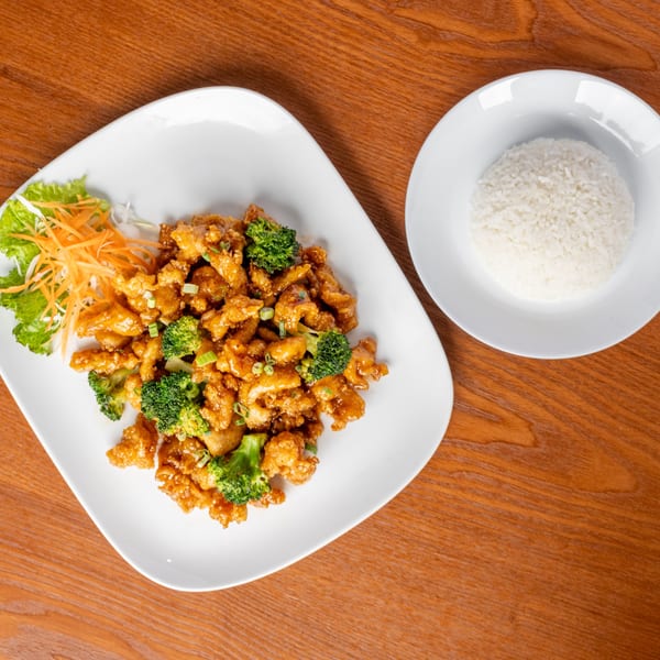 Thai orange chicken with broccoli and green onions, served with a side of white rice.