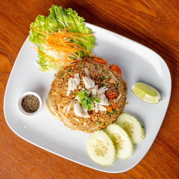Thai crab fried rice with carrots, peas, and cilantro, served with lime, cucumber, and pepper.