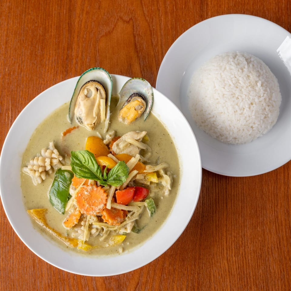 Thai green curry with mussels, squid, vegetables, and basil, served with a side of white rice.