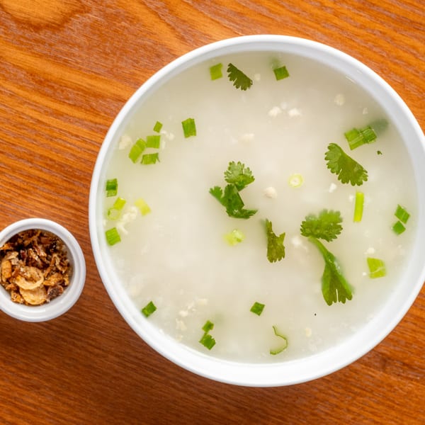 Overhead view of a Thai rice porridge with green onions and cilantro, next to a small bowl of crispy garlic.
