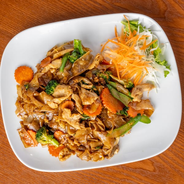 Thai Pad See Ew with chicken, broccoli, carrots, and snap peas on a white plate.